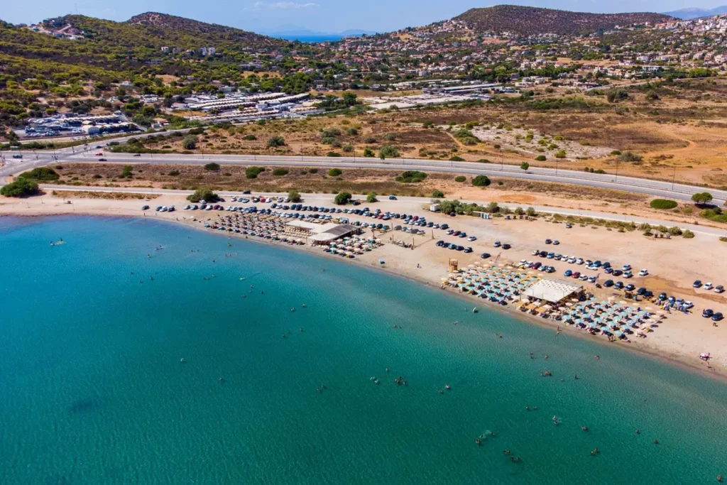 Aerial view of a long sandy beach, umbrella rows and swimmers in the Anavyssos bay.
