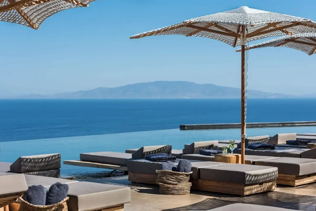 Cushioned loungers and straw umbrellas on Andronis Arcadia’s pool terrace, with the sea beyond.