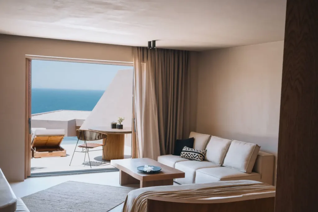 Neutral-toned suite with a sofa and open doorway to a pool terrace and sea view at Andronis Arcadia.