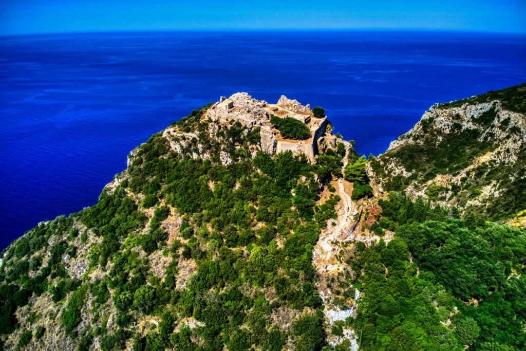Stone fortress ruins crown a steep green hill above the deep-blue sea at Angelokastro