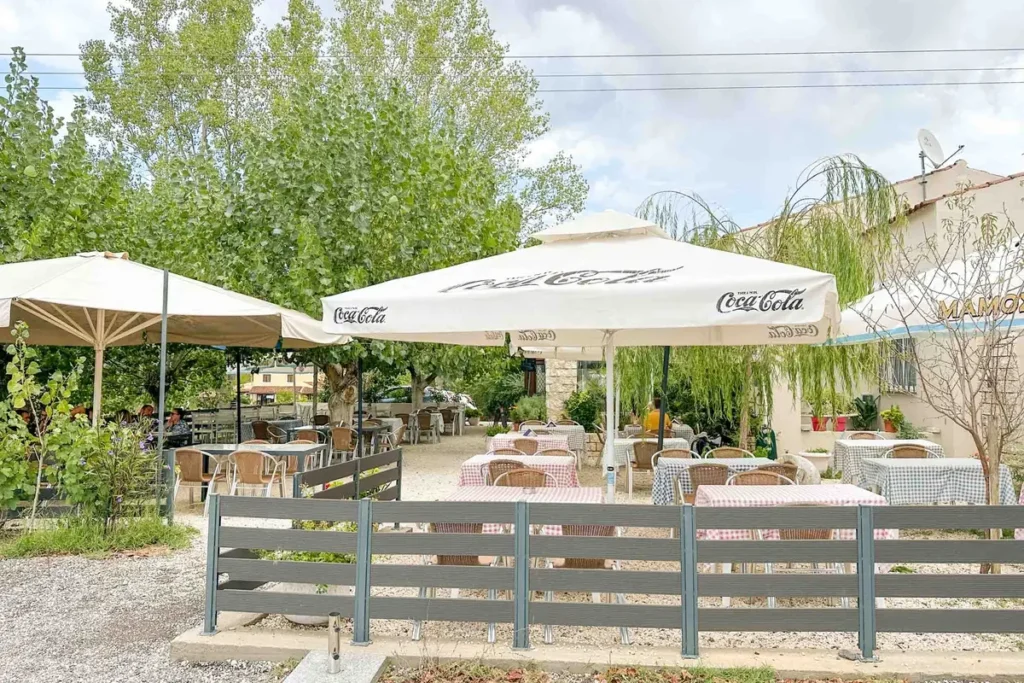 Outdoor tables beneath white umbrellas, surrounded by trees and plants at Apomero