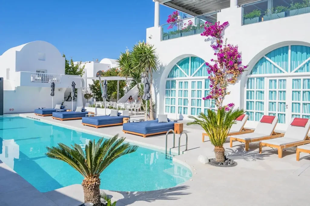 Swimming pool surrounded by white buildings, blue cushions and plants at Aressana in Fira.