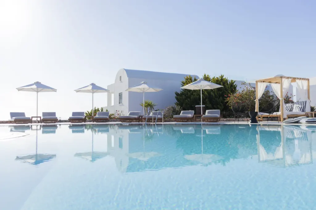 Broad swimming pool beside white buildings and loungers at Astro Palace in Santorini.