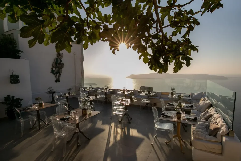 Tables set beneath a tree on a sea-facing terrace at Athenian House in Santorini.