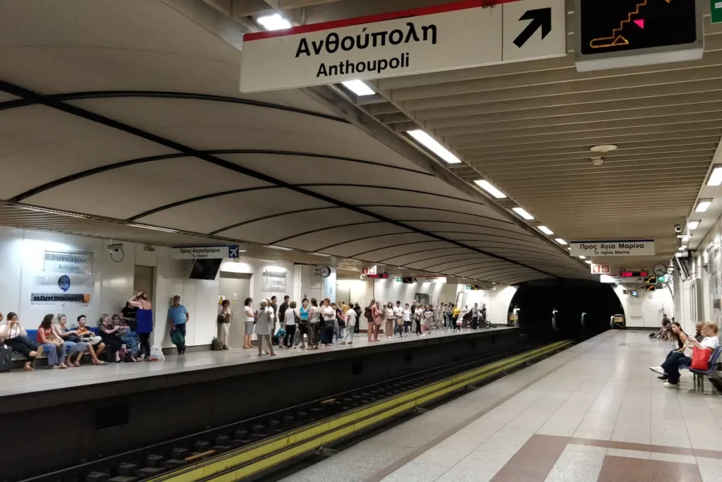 Passengers wait on Syntagma’s Metro platforms beneath directional signs and curved ceiling panels.