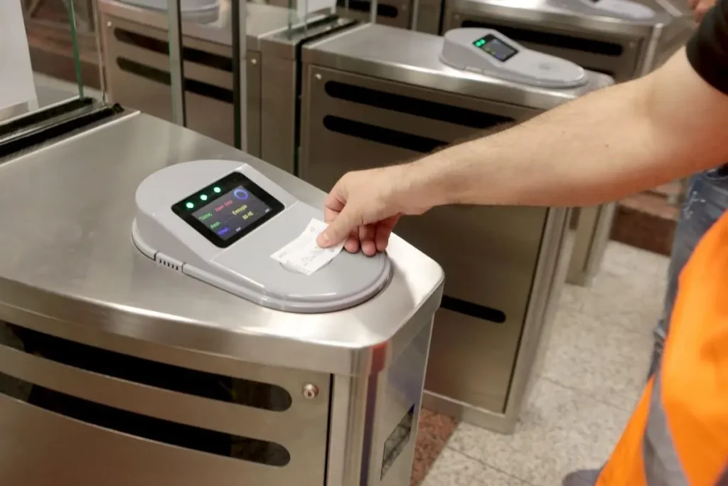 A passenger holds a paper ticket against the contactless reader on an Athens Metro gate.