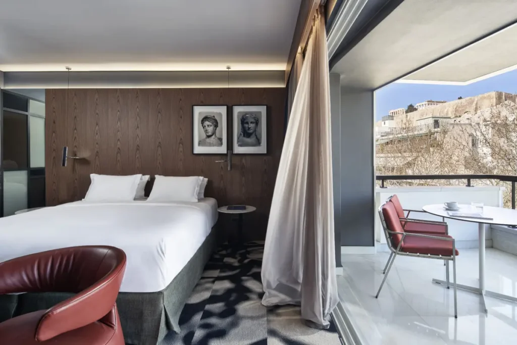 A dark-wood bedroom at AthensWas opens onto a balcony facing the Acropolis.