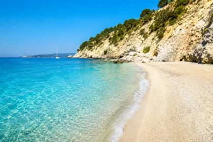 Clear turquoise water and a quiet beach beneath limestone cliffs in Greece