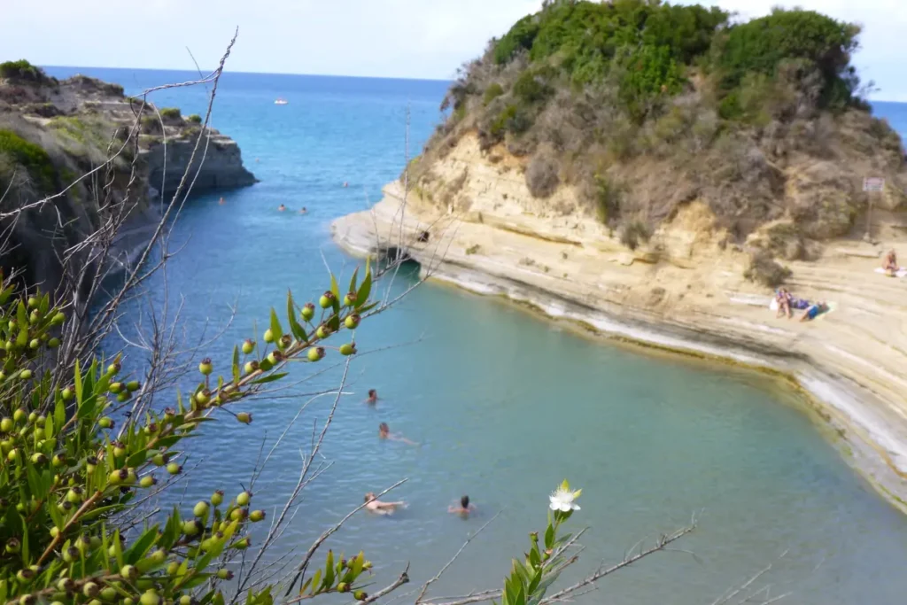 Swimmers enter a narrow channel bordered by layered sandstone cliffs at Canal d'Amour
