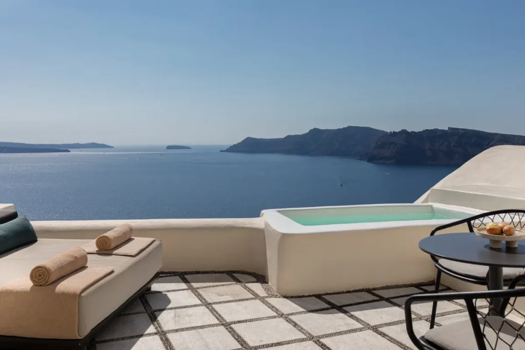 Loungers, a round dining table, and a plunge pool overlooking the caldera at Canaves Oia Suites in Santorini.