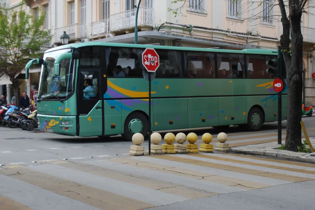A green intercity coach passes buildings and a pedestrian crossing in Corfu Town