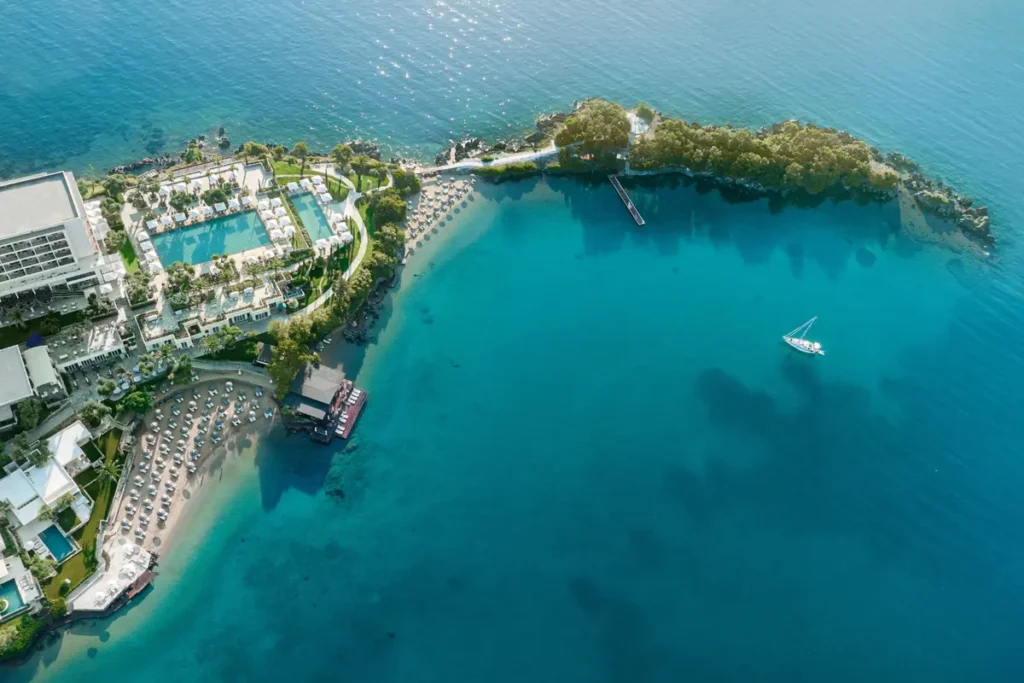 Aerial view of Corfu Imperial's buildings, pools and sheltered coastline on the Kommeno peninsula