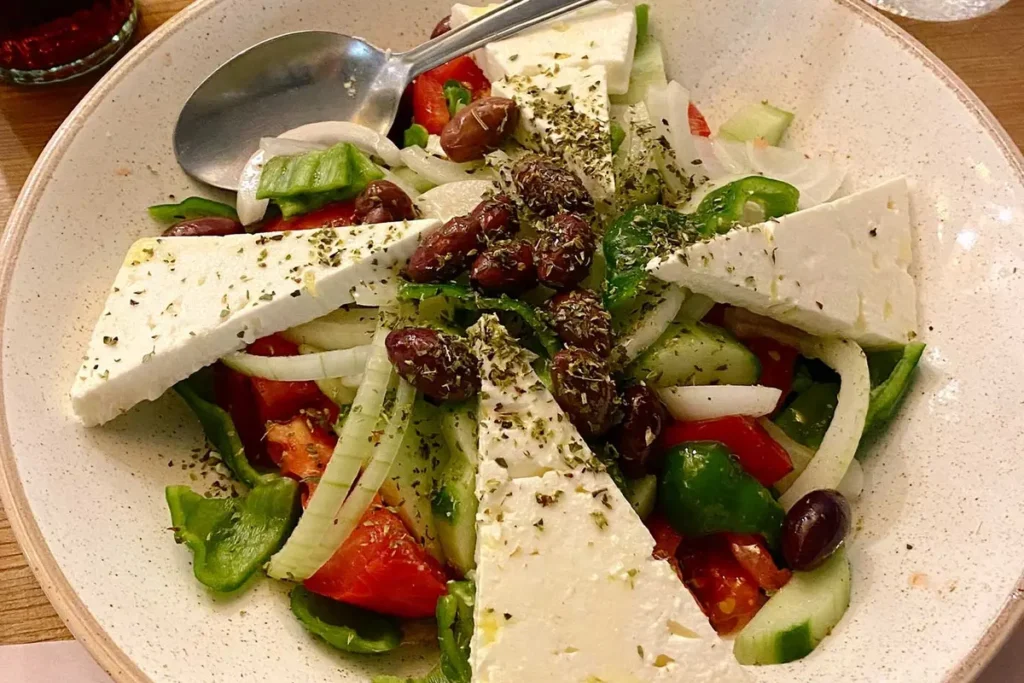 A bowl of Greek salad topped with feta and herbs on a restaurant table