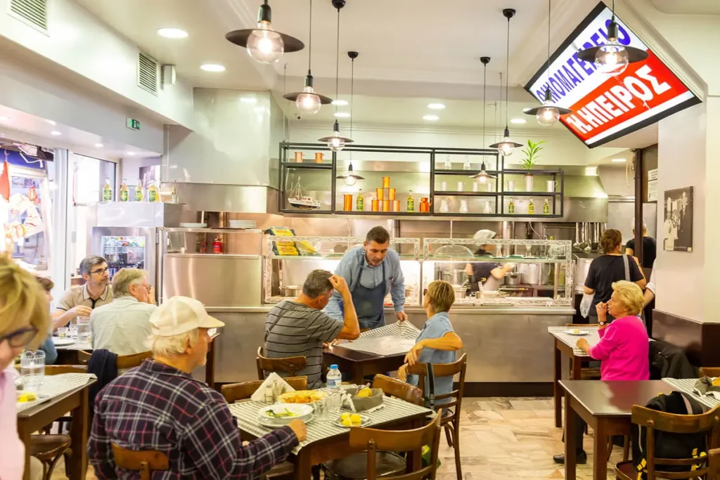 Diners sit at checkered tables beside Epirus’s prepared-food counter inside Athens Central Market.