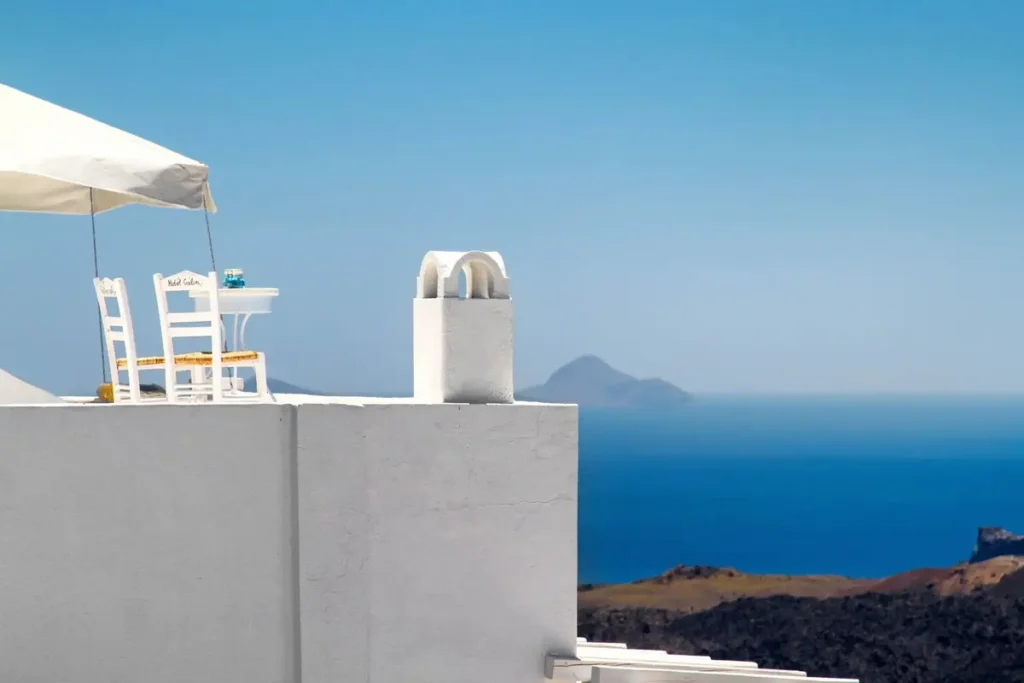 White chairs beneath an umbrella on a terrace overlooking the blue caldera in Firostefani.