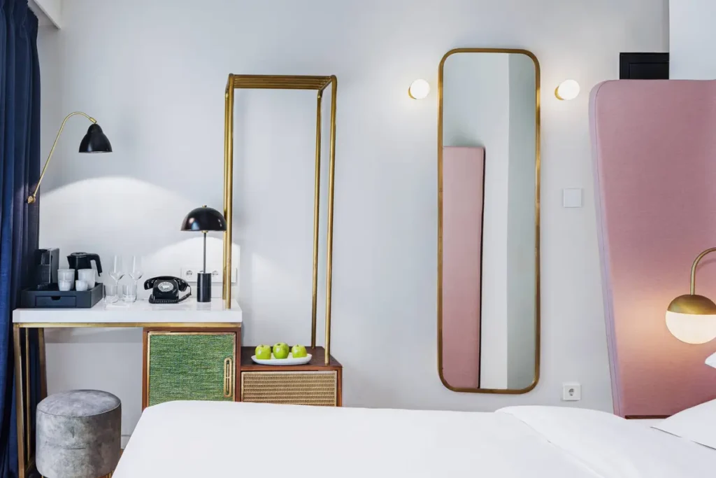 A pink headboard, curved mirrors and brass-toned fittings in a Gatsby Athens guest room.