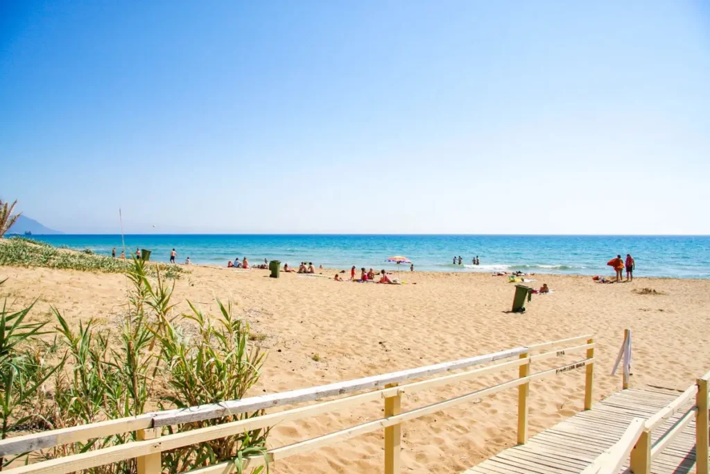 A wooden access ramp leads onto Glyfada's broad sandy beach beside blue water