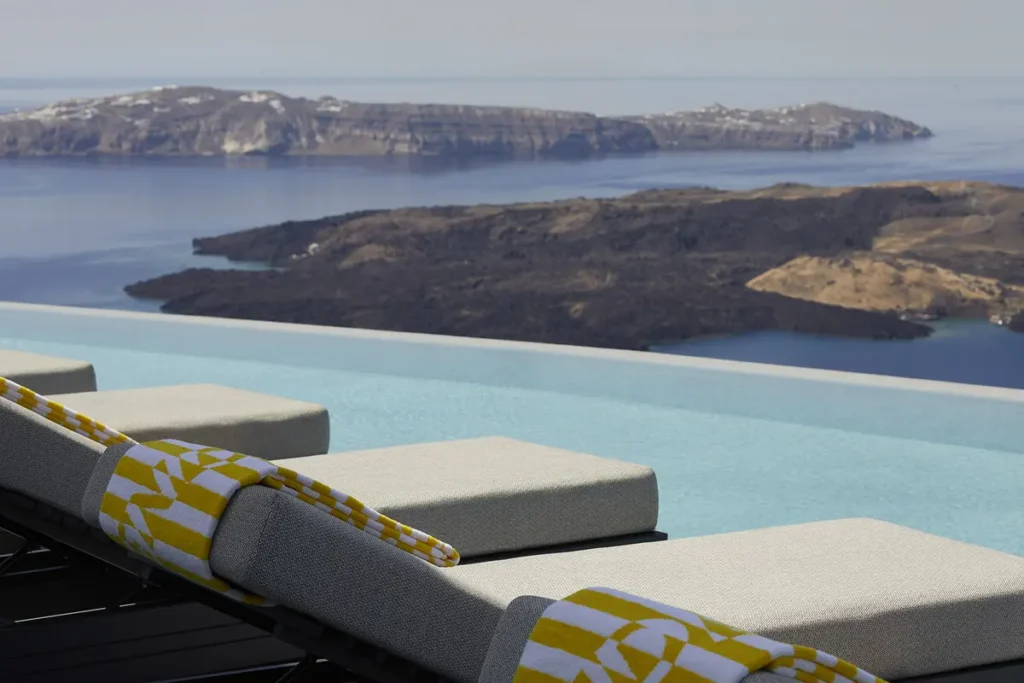 Infinity pool and a row of sun loungers overlooking the caldera at Grace Hotel in Santorini.