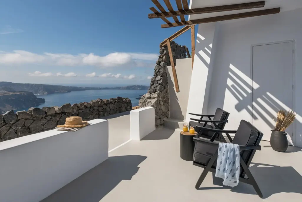 Two black chairs on a white terrace framed by dark volcanic stone at Honeymoon Petra Villas in Santorini.