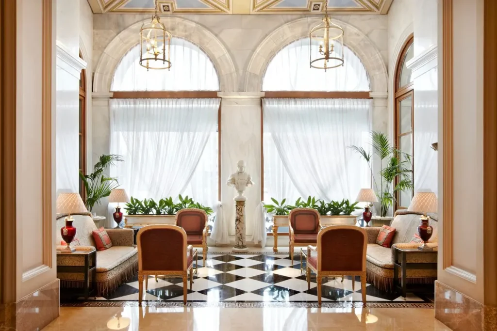 Arched windows, chandeliers and upholstered chairs around the patterned marble floor of the Winter Garden.