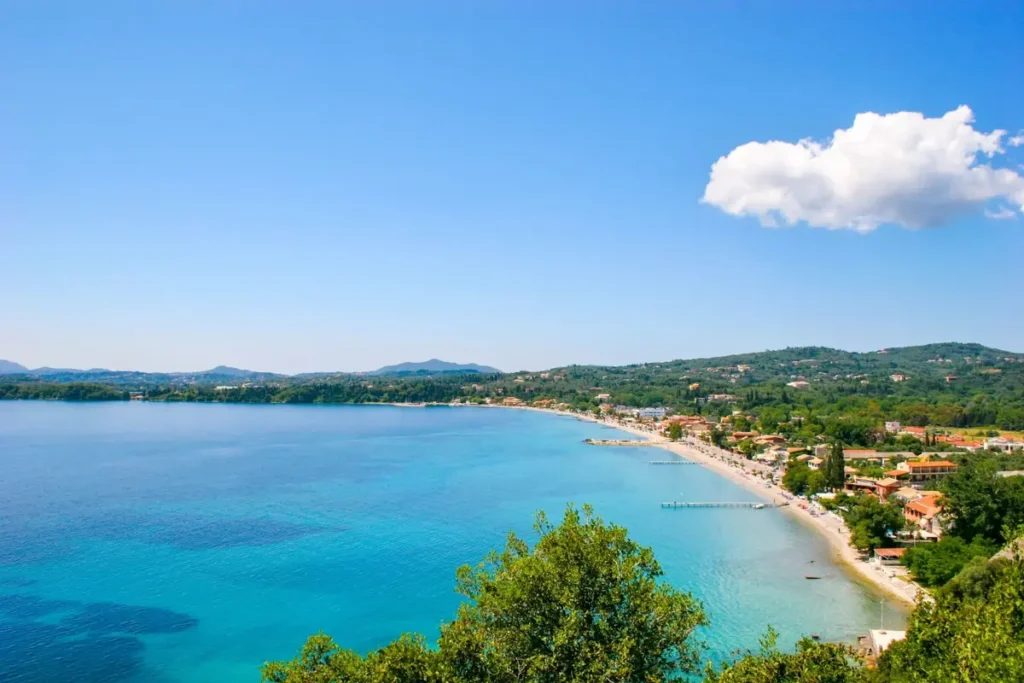 A sweeping blue bay with a narrow beach and buildings along the shore at Ipsos