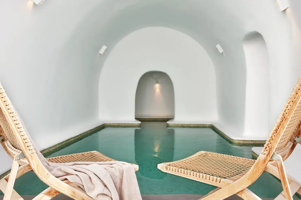 Two suspended chairs beside a pool beneath a white vaulted ceiling at the Kirini spa.