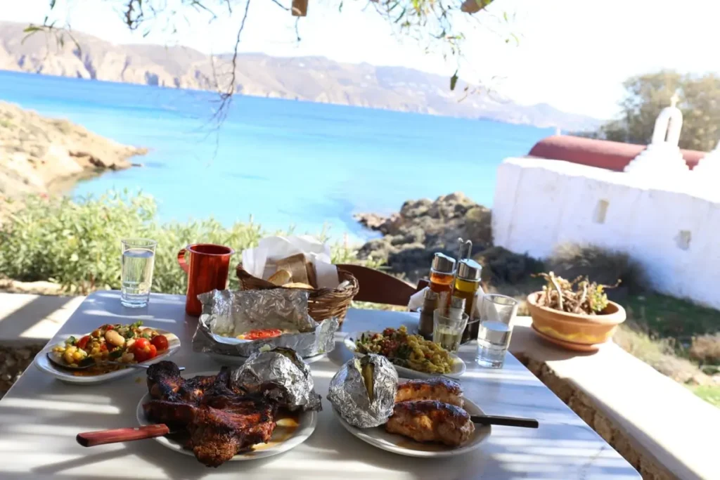 Grilled dishes, foil-wrapped potatoes and salads on a shaded table overlooking the sea at Kiki's Tavern