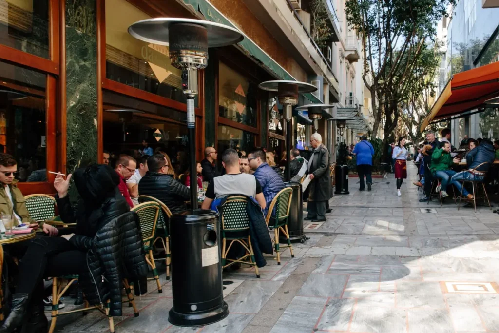 Guests sit at café tables beneath trees along a pedestrian street in Kolonaki.