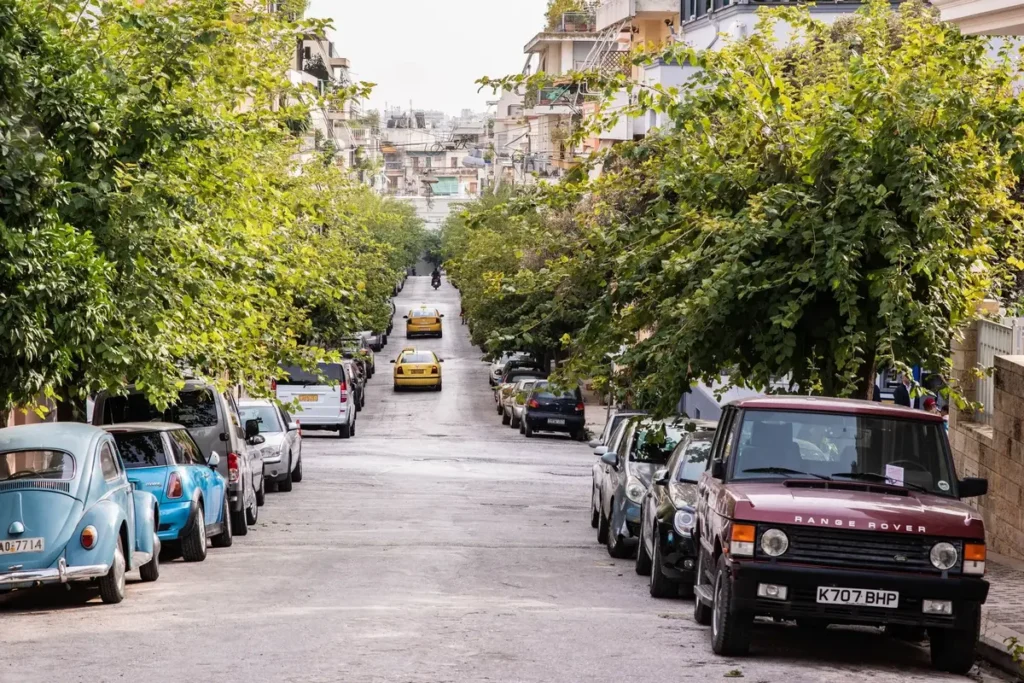 A tree-lined residential street in Koukaki with apartment buildings and parked cars.