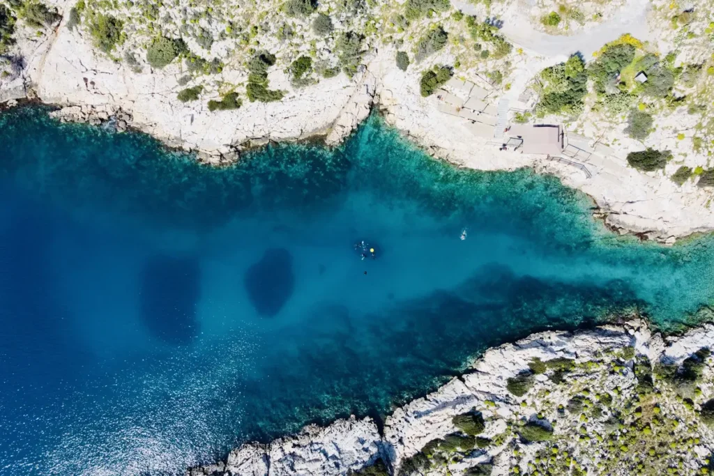 An overhead view of a deep-blue cove bordered by pale rocks at Limanakia Vouliagmenis.