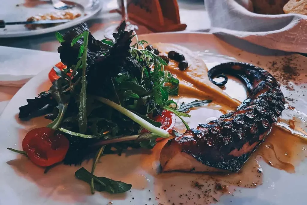 Grilled octopus served with leafy greens and sauce at Metaxi Mas in Santorini.