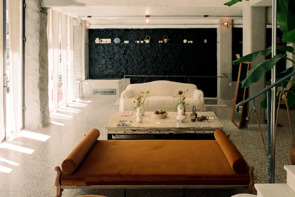 A vintage sofa and low marble table sit in Mona’s bright living room with exposed structural details.