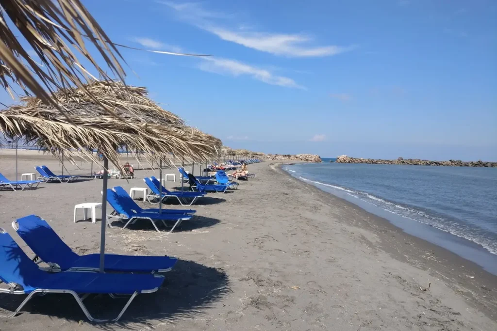 Blue loungers under straw umbrellas on the broad sandy shore at Monolithos Beach.