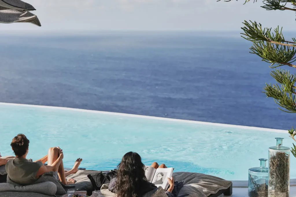Two guests reclining beside an infinity pool overlooking the sea at Myconian Utopia