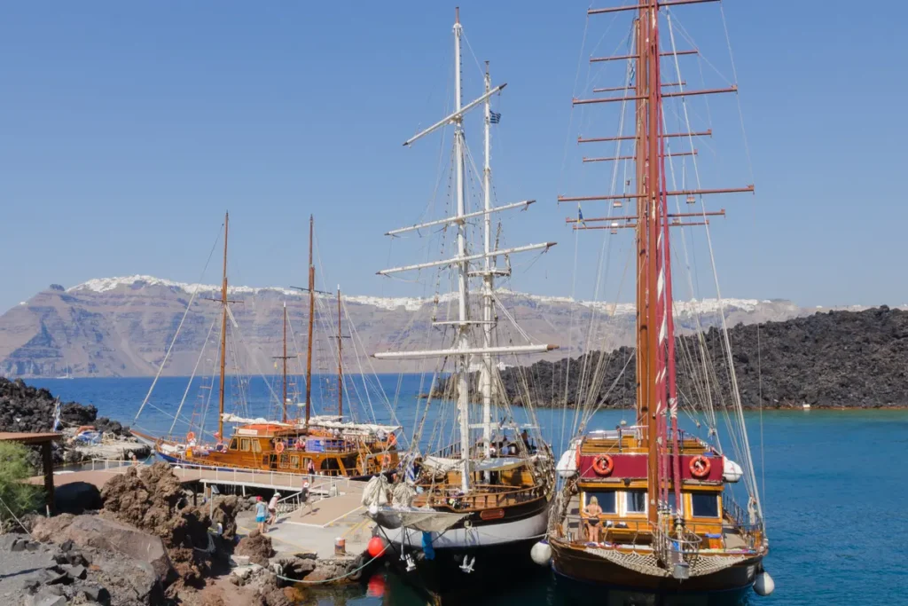 Wooden tour boats moored beside the dark volcanic rocks of Nea Kameni in Santorini.