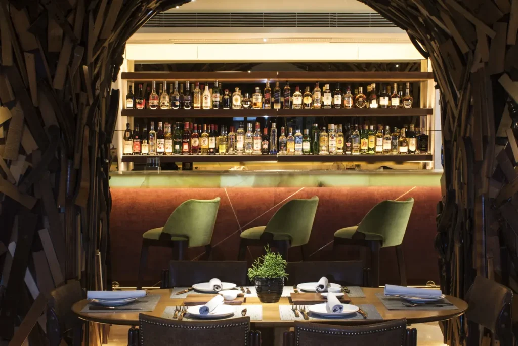 Wooden sculptural partitions frame a set dining table and illuminated bar at NEW Hotel.