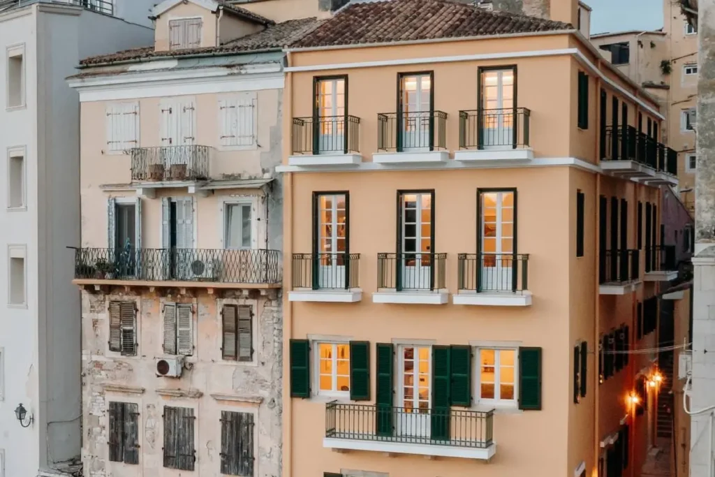 The colorful multi-story facade of New York Luxury Suites beside neighboring Corfu Town buildings