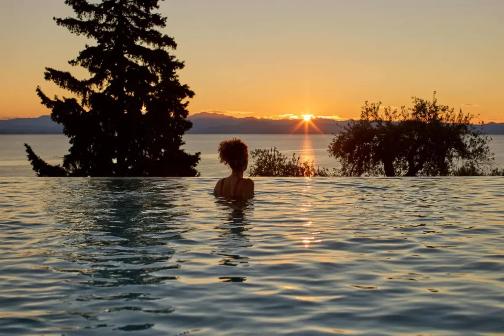 A swimmer rests in a sea-facing pool as low sunlight glows between the trees at Nido