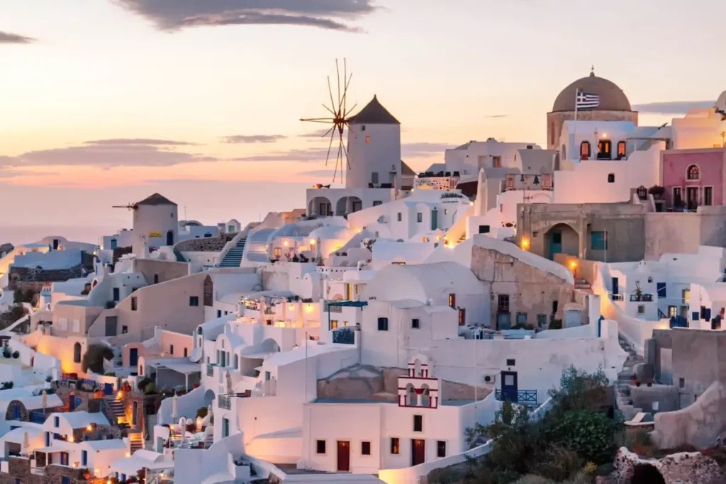 Whitewashed houses, a windmill and a church in Oia beneath a softly lit evening sky.