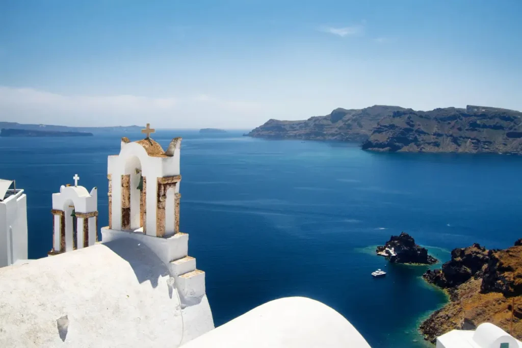 White bell tower above blue caldera water and cliffside buildings in Oia.