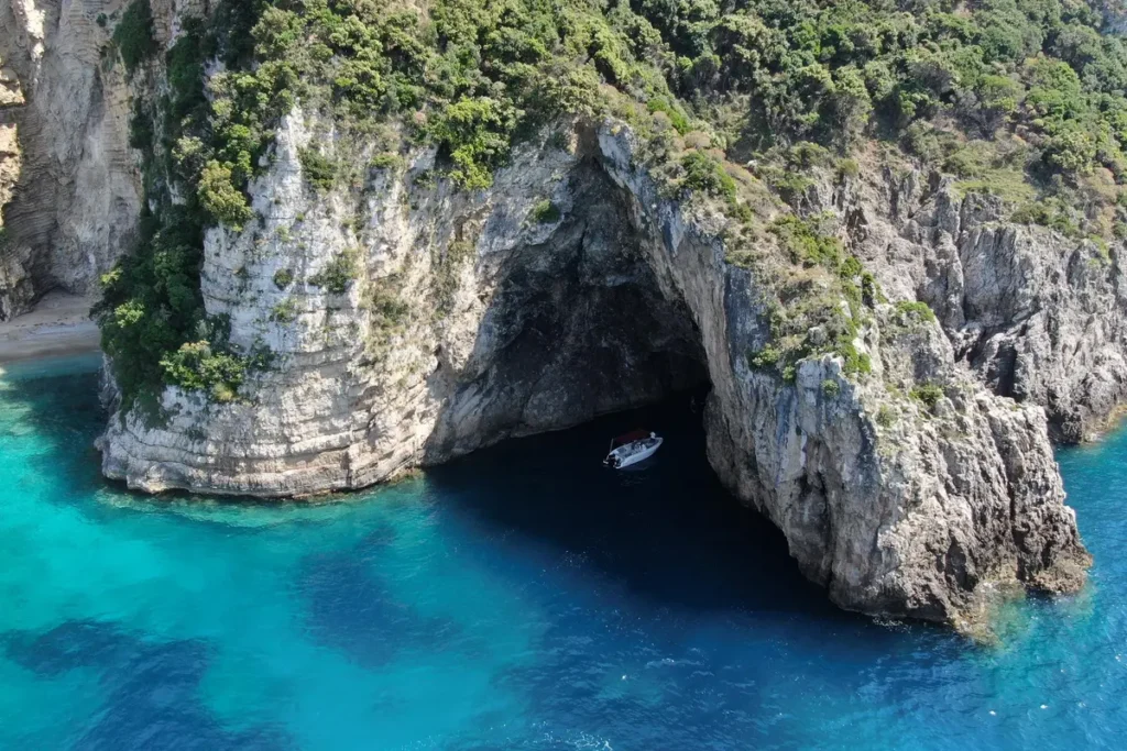 A dark sea-cave entrance opens beneath a steep rocky cliff beside turquoise water