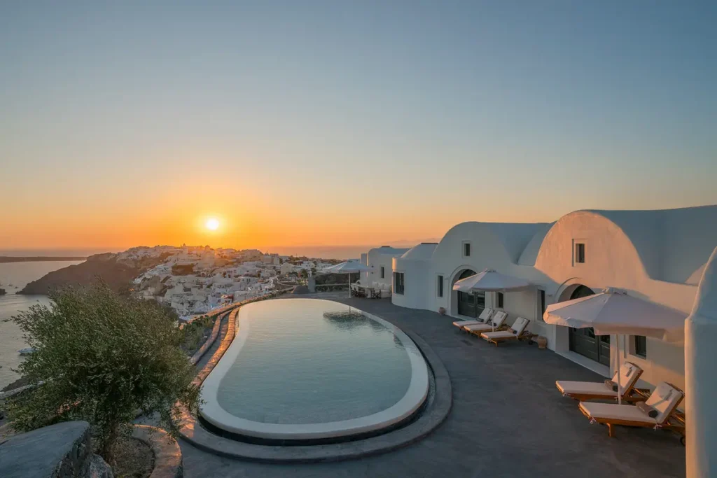 Curved infinity pool beside white buildings and sun loungers at Perivolas in Oia.