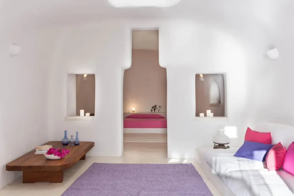 White cave-style living room with pink and purple cushions and a bedroom alcove at Perivolas, Santorini.