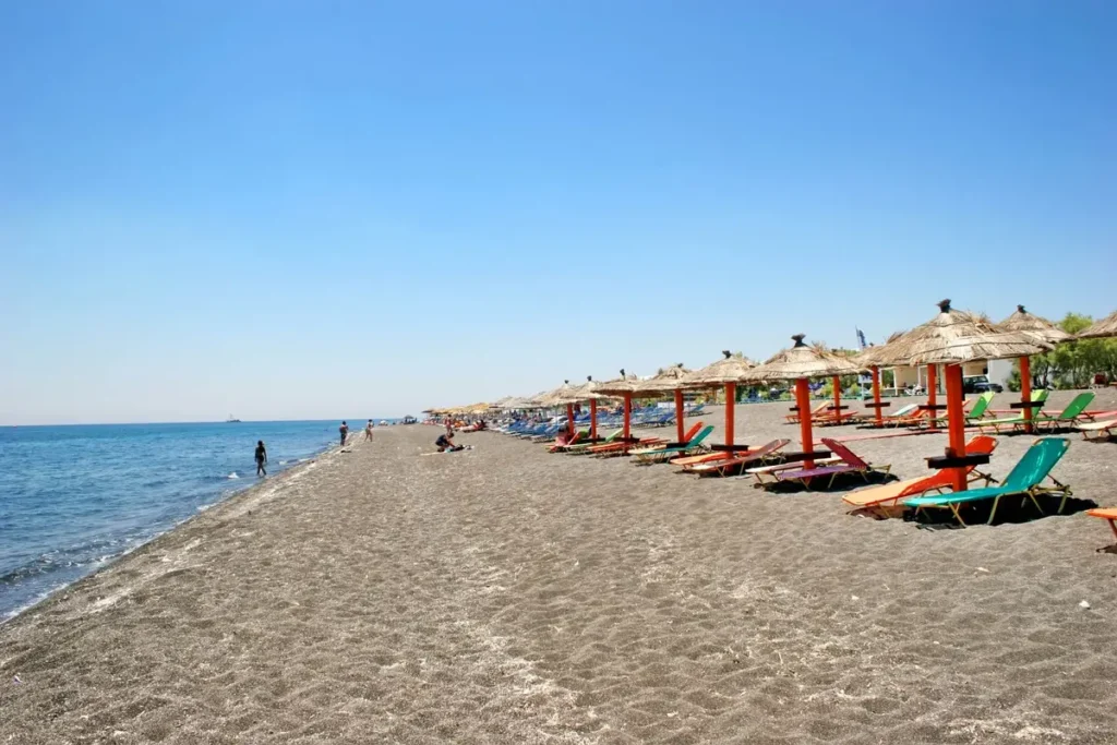 Rows of loungers and umbrellas along the dark volcanic beach at Perivolos.
