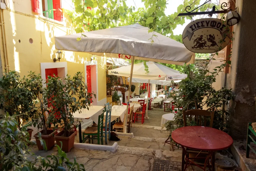 Restaurant tables and umbrellas line a stepped lane between colorful buildings in Plaka.