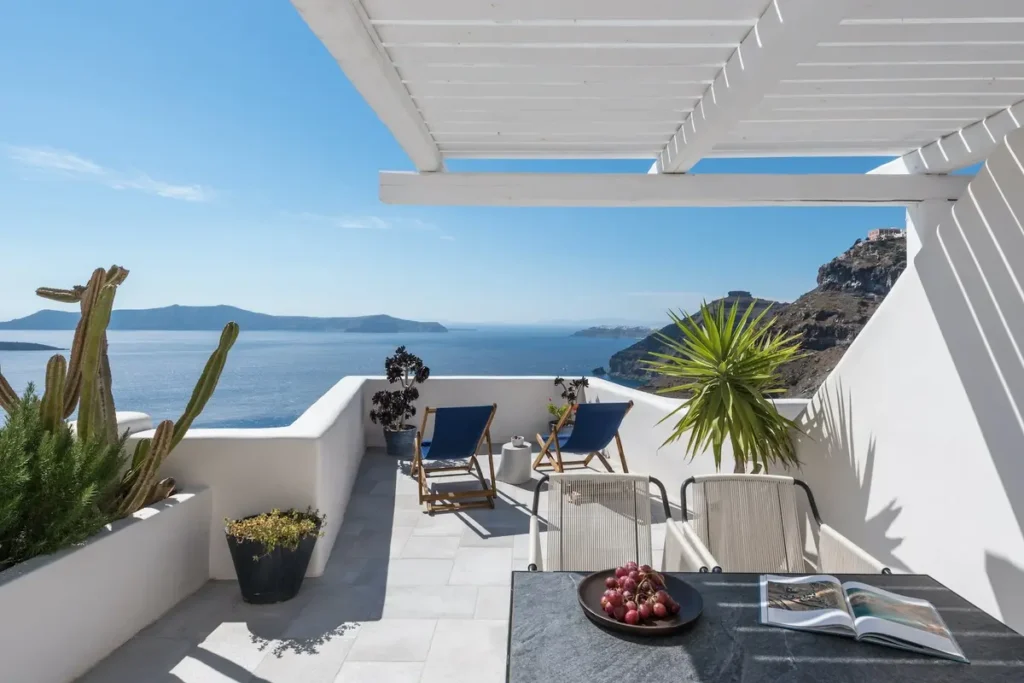 A shaded terrace with outdoor seating and a table overlooking the caldera at Porto Fira Suites.