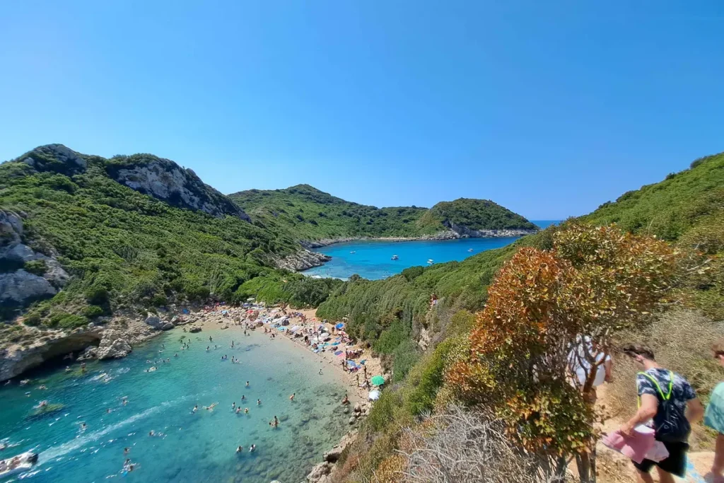 Two turquoise coves separated by a narrow strip of land, seen from a rocky trail above Porto Timoni