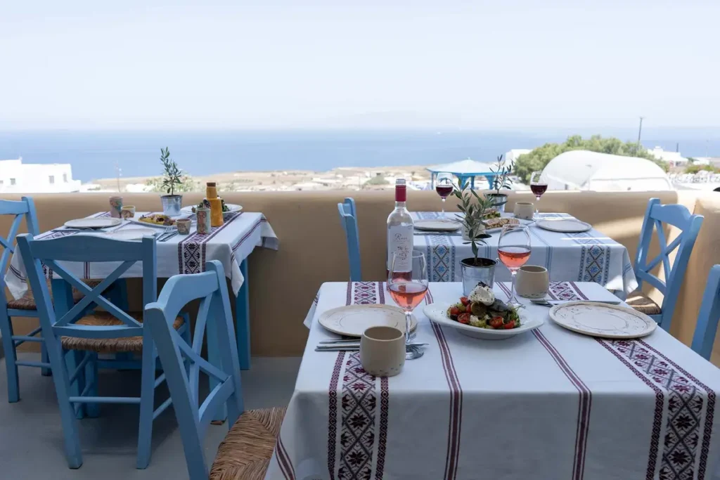 White tables and blue chairs on Roka’s outdoor terrace in Oia.