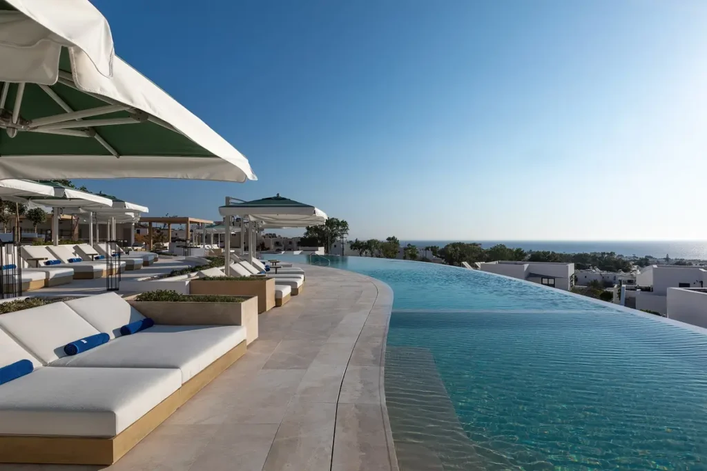 Curved infinity pool with shaded loungers and sea views at Sandblu Santorini.
