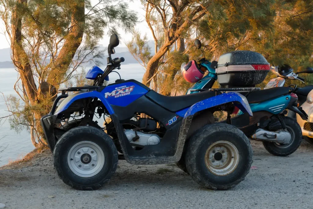 Blue quad bike parked on gravel beneath trees in Santorini.